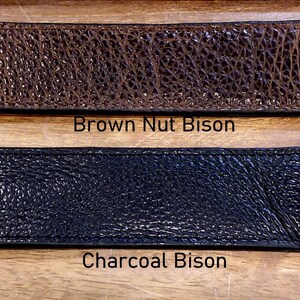 May include: Two rectangular leather strips with rounded ends and stitched edges. The top strip is textured brown leather labeled Brown Nut Bison. The bottom strip is textured black leather labeled Charcoal Bison. Both items feature a pebbled surface.