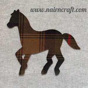 Peut inclure: Une applique en tissu en forme de cheval, présentant un motif à carreaux marron, noir et beige avec une rayure rouge sur la queue. Le texte www.nairncraft.com est imprimé dans le coin supérieur droit au-dessus de la silhouette du cheval.