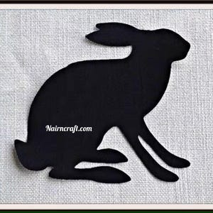 May include: A solid black silhouette of a hare in a seated position, featuring long ears and a curved back. The text Nairncraft.com is printed in white across the center of the hare's body. The design is presented against a textured white background.