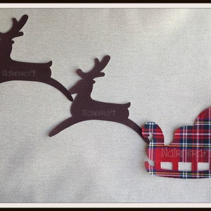 May include: Two dark brown reindeer silhouettes and one red, blue, and white plaid patterned sleigh cutout. Each of the three shapes features the word Nairncraft embossed in the center. The items are arranged in a horizontal line.