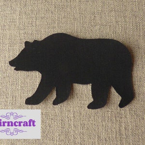 May include: A black bear silhouette cutout made of fabric with a visible woven texture. In the bottom left corner, a rectangular white label features the purple text Nairncraft with decorative flourishes above and below the brand name.