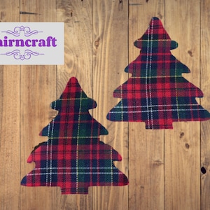 May include: Two fabric cutouts shaped like Christmas trees featuring a red, green, and white plaid pattern. The text "Nairncraft" is printed in purple on a light grey rectangular background in the upper left corner of the image.