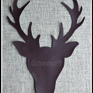 May include: A dark brown, textured deer head silhouette cut from leather-like material, featuring prominent antlers and pointed ears. The word Nairncraft is embossed in the centre of the deer head, which is displayed against a neutral grey fabric.
