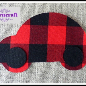 Peut inclure: Une découpe en tissu en forme de voiture avec un motif à carreaux rouge et noir et deux roues circulaires noires unies. Le texte Nairncraft est imprimé en violet sur un fond rectangulaire gris clair dans le coin supérieur gauche.