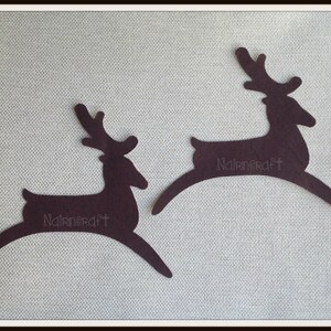 May include: Two dark brown, flat, die-cut felt shapes in the silhouette of leaping reindeer. Each reindeer figure features a small, stylized antler design and the text "Nairncraft" printed in a light, thin font across the centre of the body.