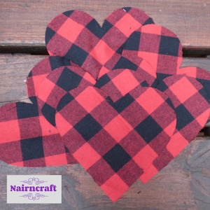 Puede incluir: Un conjunto de recortes de tela en forma de corazón con un patrón de cuadros rojos y negros. Los corazones están superpuestos y una etiqueta rectangular blanca en la esquina inferior izquierda muestra el texto morado Nairncraft.