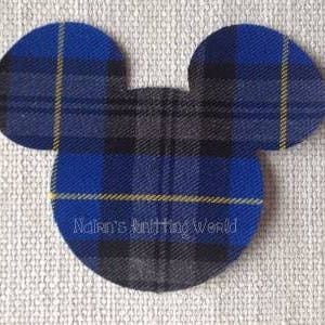 May include: A fabric cutout shaped like a mouse head featuring a blue, black, and grey plaid pattern with thin yellow lines. The text Nalan's knitting world is printed in white across the lower section of the circular head shape.