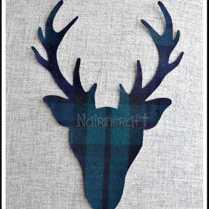 May include: A fabric cutout in the shape of a deer head with antlers, featuring a dark blue and green plaid tartan pattern. The word Nairncraft is printed in a light, thin font across the center of the deer head shape.