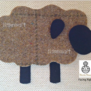 May include: A sheep-shaped appliqué made of brown tweed fabric with a textured weave. It features a solid black fabric head, ear, and four rectangular legs. The text Nairncraft is visible twice on the body, and a Harris Tweed logo is present.