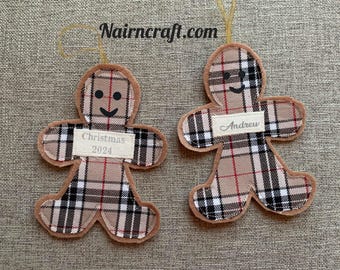 May include: Two gingerbread man ornaments made of beige, black, and red plaid fabric with tan felt borders. Each has a black stitched smile and eyes. One features a white label reading Christmas 2024, the other reads Andrew. Gold hanging loops.