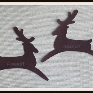 May include: Two dark brown, flat, silhouette-style reindeer cutouts in a leaping pose. Each reindeer features a textured surface and the word Nairncraft printed in a light, thin font on the body. The figures are oriented in opposite directions.