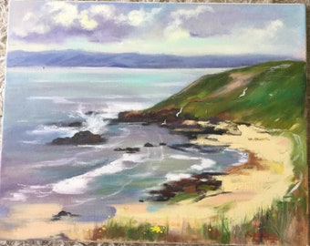 May include: A painting depicting a seascape with a rocky coastline, a sandy beach, and a green hill in the background. The sky is a light blue with white clouds. The water is a light blue and green colour, and the waves are crashing on the rocks.