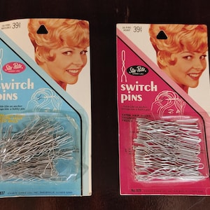 May include: Two vintage packages of Sta-Rite Switch Pins. One package is blue and the other is pink. Each package features a smiling woman with blonde hair. The packages contain silver-colored bobby pins. The text "SWITCH PINS" is prominently displayed on each package.