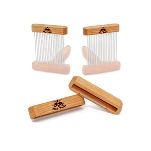 May include: Two wooden combs with metal teeth and a wooden block with the text "Fiber Works" on it. The combs are used for carding wool or other fibers.