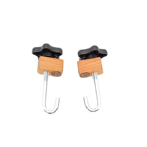 May include: Two wooden clamps with black knobs and metal hooks. The clamps have a brown wood finish and are designed to hold objects securely.