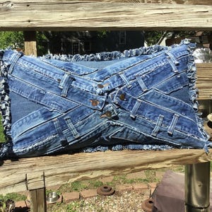 Denim throw pillow, sham style with pillow insert included. Uses recycled jean front waistband fasteners arranged in an X shape arrangement