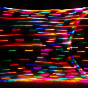 May include: Abstract image of colorful, blurred lines of light against a black background. The lines are arranged in a grid pattern, creating a dynamic and energetic visual.