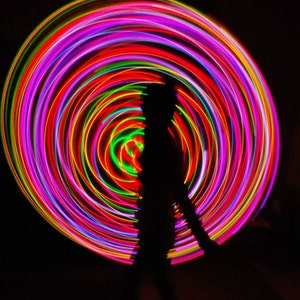 May include: A silhouette of a person standing in front of a colorful, swirling light display. The light display is made up of concentric circles of red, pink, green, and yellow.