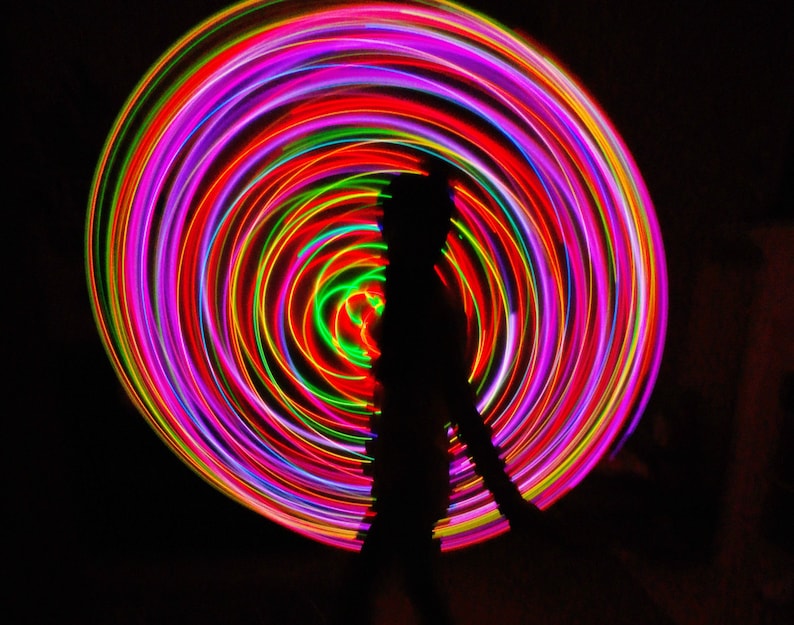 May include: A silhouette of a person standing in front of a colorful, swirling light display. The light display is made up of concentric circles of red, pink, green, and yellow.