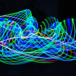 May include: Abstract light painting with swirling lines of blue, green, red, and white light on a black background.