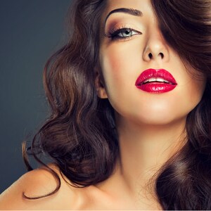 May include: A woman with long, dark brown hair styled in loose curls. Her hair is parted on the side and falls over one eye. She is wearing red lipstick and has a neutral makeup look.