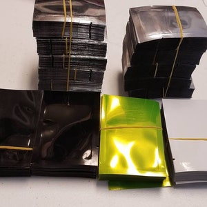 May include: Stacks of various colored plastic bags, including black, silver, green, and white. The bags are all sealed with rubber bands.