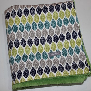 May include: A green and white baby blanket with a leaf pattern and a gray label that says "Little Bloom".