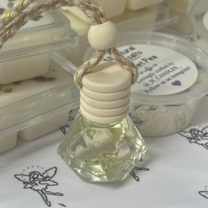 May include: A clear glass car air freshener in a diamond shape with a wooden cap and a gold string. The air freshener is labelled "H Candles" and the scent is "Sweet Pea".