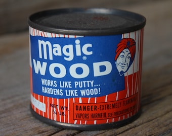 Op de afbeelding: Een blauwe en rode blik Magic Wood, een houtvullerproduct. De blik heeft een rood-wit gestreepte achtergrond met een cartoonman met een tulband op de voorkant. De tekst op de blik luidt "Magic Wood", "Works like putty... Hardens like wood!" en "Danger - Extremely Flammable. Vapors Harmful. See Precautions on Back."