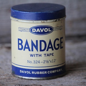 May include: Vintage Davol Bandage tin with a blue lid and base, and a cream-colored body. The tin reads "BANDAGE WITH TAPE" in blue lettering, along with the dimensions "2-½"x12'". The Davol Rubber Company logo is also visible.