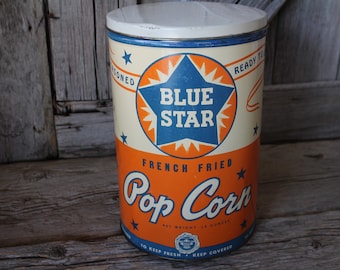 May include: A vintage metal tin for Blue Star French Fried Popcorn. The tin is orange, white, and blue with a large blue star and the words "Blue Star" in white. The text "French Fried Pop Corn" is in a white cursive font on an orange background. The tin has a white lid and a net weight of 13 ounces.