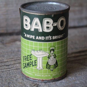 May include: A vintage green and white tin can with the text "BAB-O" and "A wipe and it's bright". The can also has a picture of a woman in a white dress and a green apron standing in front of a white porcelain sink. The text "FREE SAMPLE" is printed on the can.