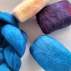 May include: A selection of colourful wool roving and felted soap bars. A large braid of bright blue wool sits beside a blue felted soap bar. There is a purple and red felted soap bar and a yellow and pink wool roving.