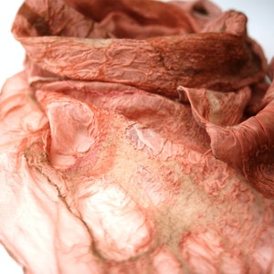 May include: A soft, peach-coloured silk scarf with a textured, crinkled design. The scarf is folded and draped, showcasing its delicate fabric and subtle colour variations.
