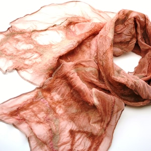 Puede incluir: Una suave bufanda de seda de color melocotón con una textura arrugada y sutiles detalles marrones y rosados.