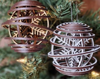 May include: Two wooden Christmas ornaments with a snowflake design. One ornament is brown and the other is white with brown accents.