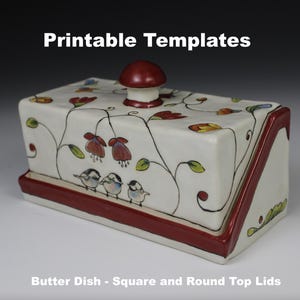 Könnte beinhalten: Eine weiße Keramik-Butterdose mit rotem Rand und floralem Design. Der Deckel hat eine runde Oberseite und einen roten Knopf. Die Dose ist mit kleinen Vögeln und Blumen verziert.