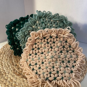 May include: Three crocheted trivets in shades of green and beige. The trivets are made with a star-shaped pattern and have a fringed edge.