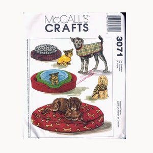May include: McCall's Crafts sewing pattern number 3071 for dog beds and coats. The pattern includes three different dog bed designs and three different dog coat designs. The dog beds are shown in red, green, and brown with various patterns. The dog coats are shown in plaid, leopard print, and a yellow solid color.