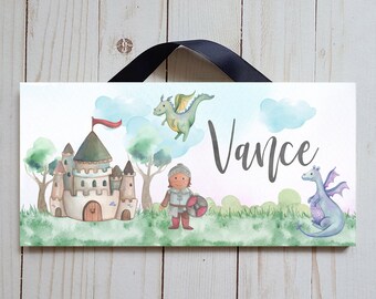 May include: A rectangular sign with a watercolor illustration of a castle, knight, and dragons. The name "Vance" is written in cursive. The sign has a black ribbon for hanging.