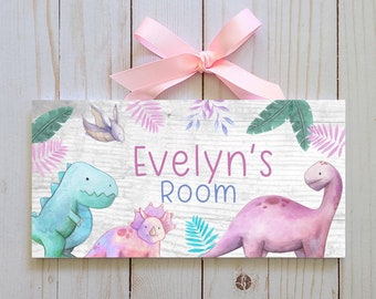 May include: A rectangular wooden sign with the text "Evelyn's Room" in purple and blue. The sign features watercolor illustrations of dinosaurs in shades of blue, pink, and purple, with green and pink foliage. A pink ribbon is attached at the top.