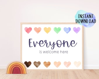 May include: A framed print with the text "Everyone is welcome here" in a handwritten font, above and below a row of watercolor hearts in various colors. A wooden rainbow toy sits on the floor in front of the print.