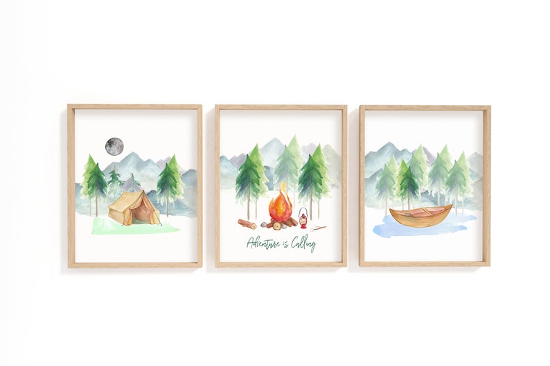 May include: Set of three framed watercolor prints featuring camping scenes. Each print depicts a different outdoor scene: a tent under a moon, a campfire, and a boat on a lake. The middle print has the text "Adventure is Calling".