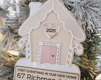 May include: A gingerbread house ornament made of light wood and white acrylic, featuring a rose gold heart with the year 2025, a pink door, and candy canes. A sign at the base reads: FIRST CHRISTMAS IN OUR NEW HOME 67 Richmond Ave.