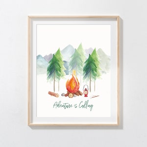 May include: Watercolor print of a campfire scene with the text "Adventure is Calling." The artwork features a campfire with flames, trees, mountains, and a lantern. The print is framed in a light wood frame.