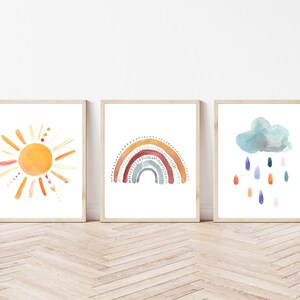 May include: Three framed watercolour art prints depicting a sun, rainbow, and rain cloud. The sun is orange with yellow rays. The rainbow has multiple colours. The rain cloud is blue with colourful raindrops.
