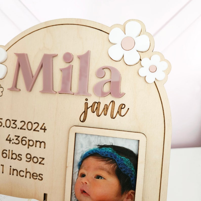 May include: Wooden baby announcement plaque with the name "Mila Jane" in pink letters, floral accents, and a photo frame. Includes birth details: date, time, weight (6lbs 9oz), and length (1 inch).