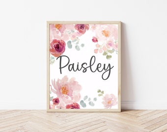 May include: A framed print featuring the name "Paisley" in elegant script. The name is surrounded by a watercolor floral arrangement in shades of pink, red, and green, creating a soft, feminine aesthetic.