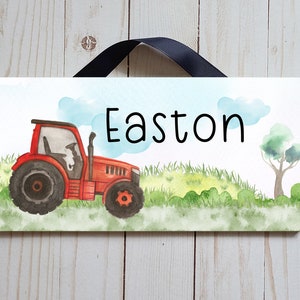 May include: A rectangular sign featuring a watercolour illustration of a red tractor in a field, with the name "Easton" in black script. The sign is suspended by a black ribbon.