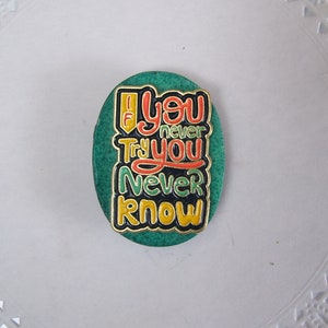May include: A green oval-shaped magnet with the text "If you never try you never know" in colorful lettering.